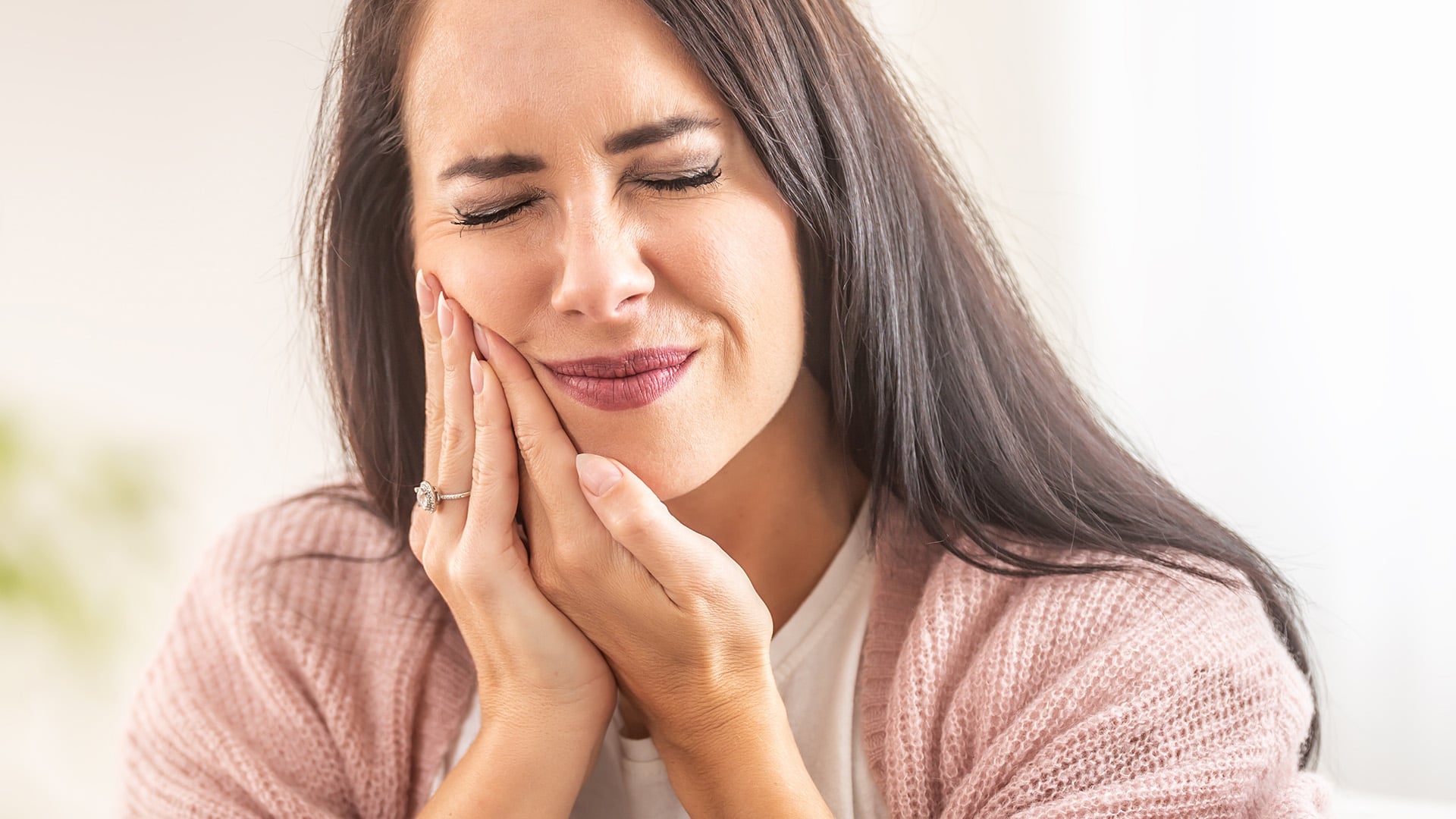 Close up image of a woman holding her cheek with an apparent tooth injury 