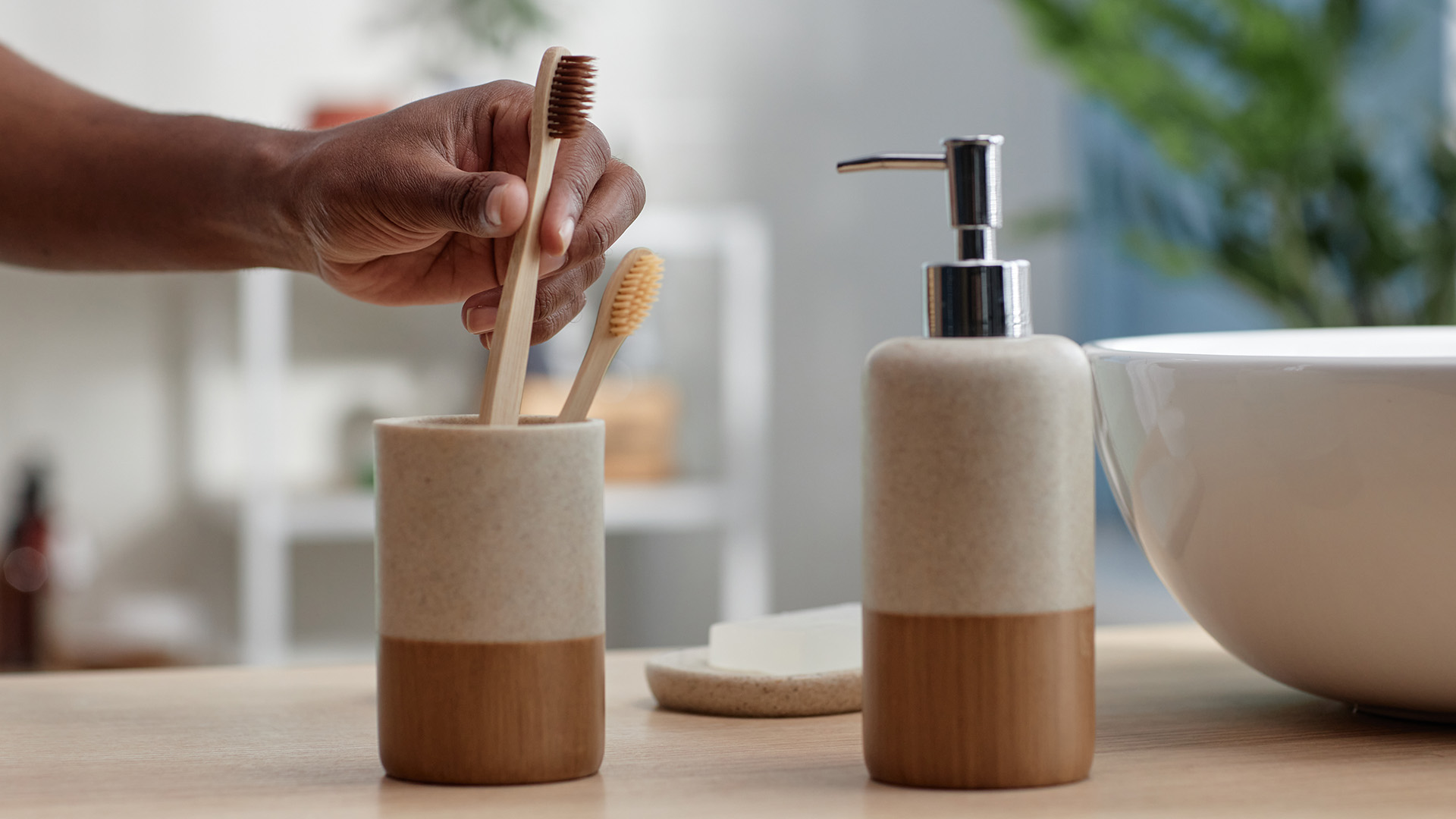 Image of a hand grabbing a wooden toothbrush out of a ceramic toothbrush holder 