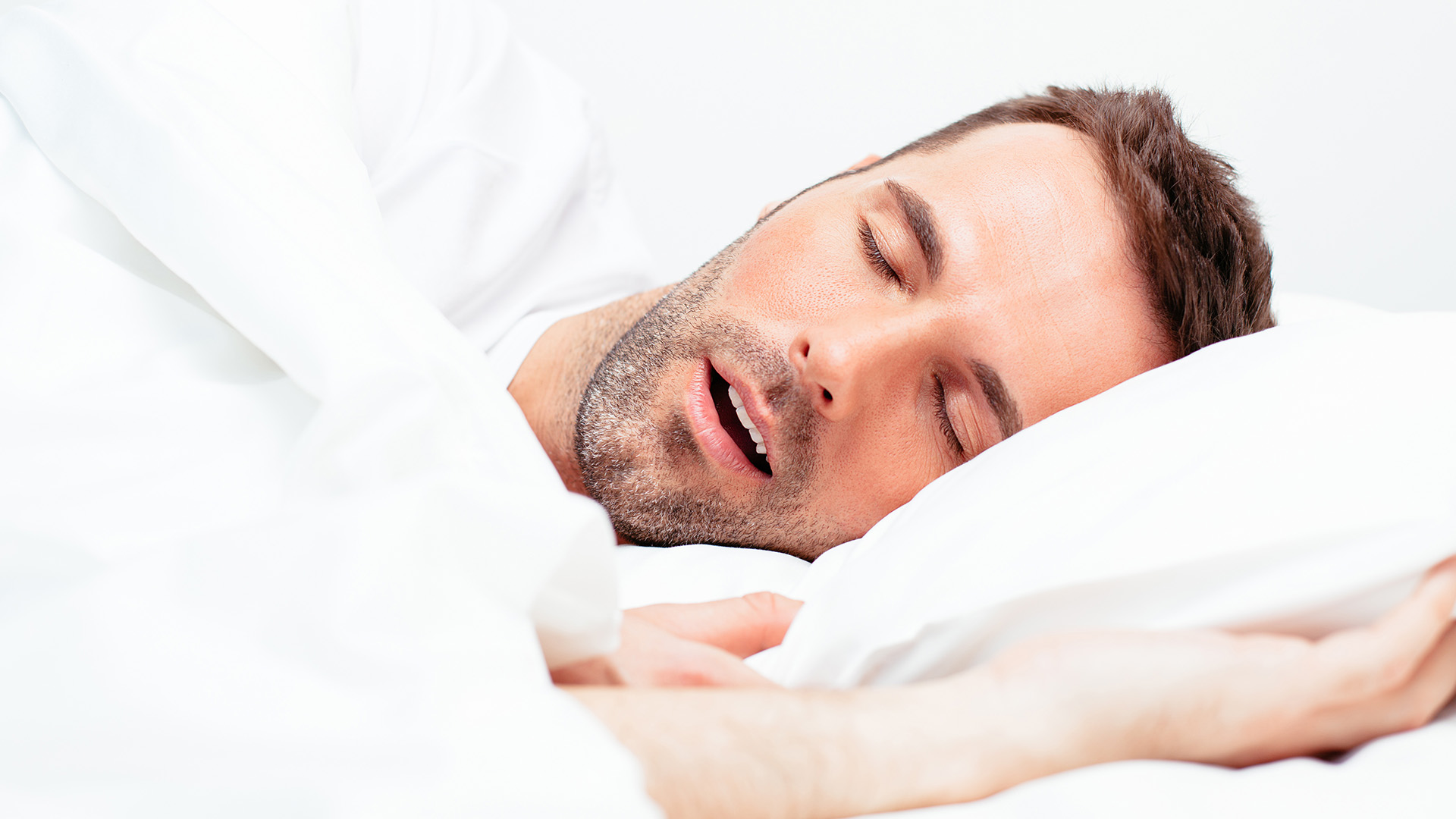 Adult man with brown hair sleeping on a pillow mid-snore 