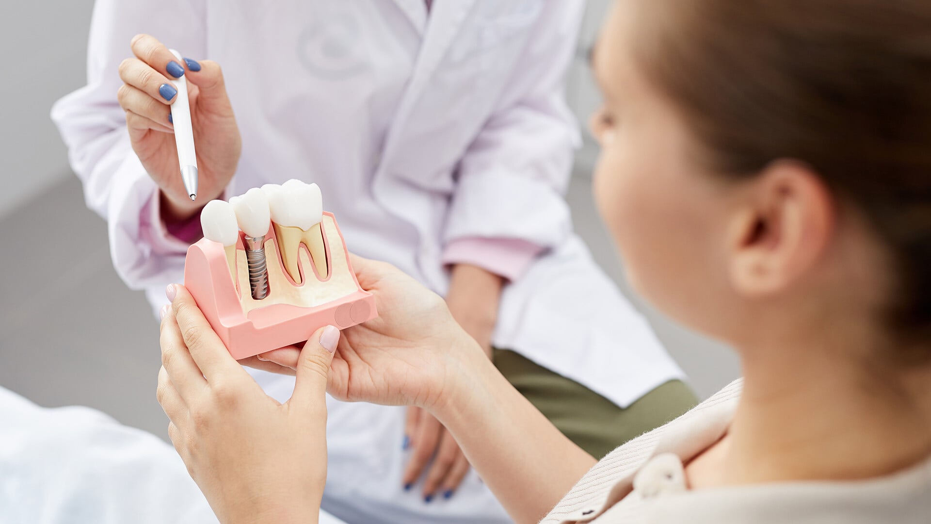 Female doctor holding a pen and pointing to a tooth model that a patient is holding which shows different implant options